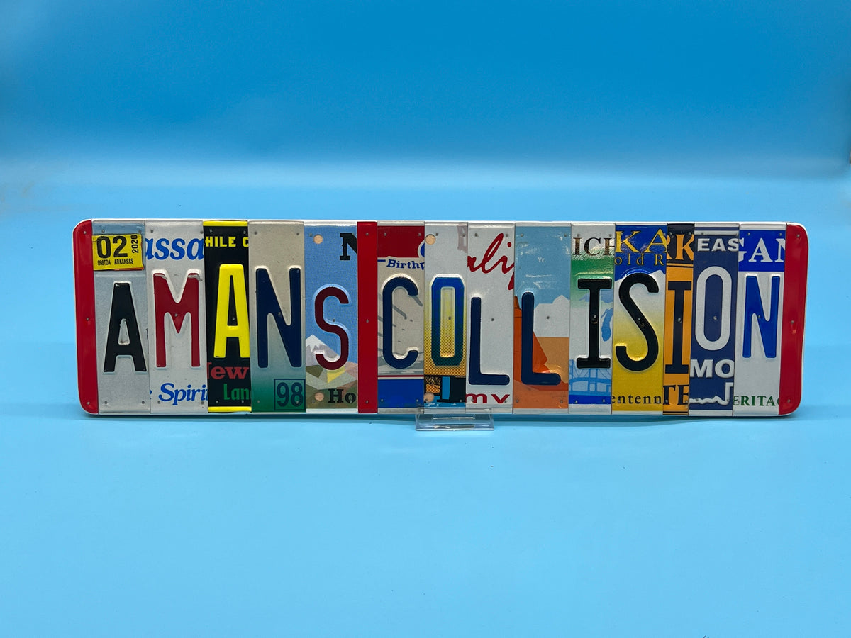 A decorative wall sign made from multiple vintage license plates spelling 'AMANS COLLISION', displayed on a small clear stand against a solid blue background.