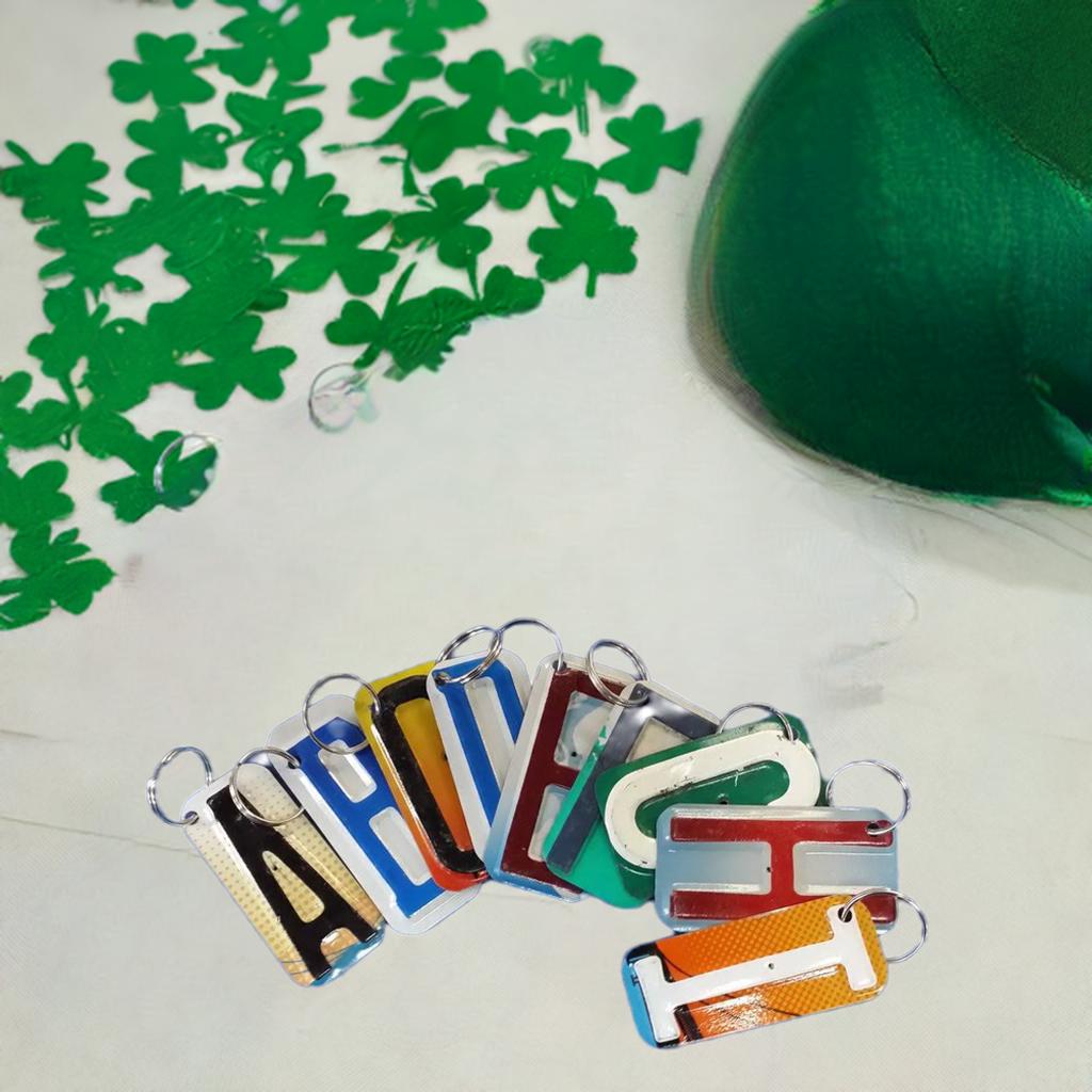 Colorful license plate letters A B C D E F G H I made into keychains on a white surface with green shamrocks and a green hat.