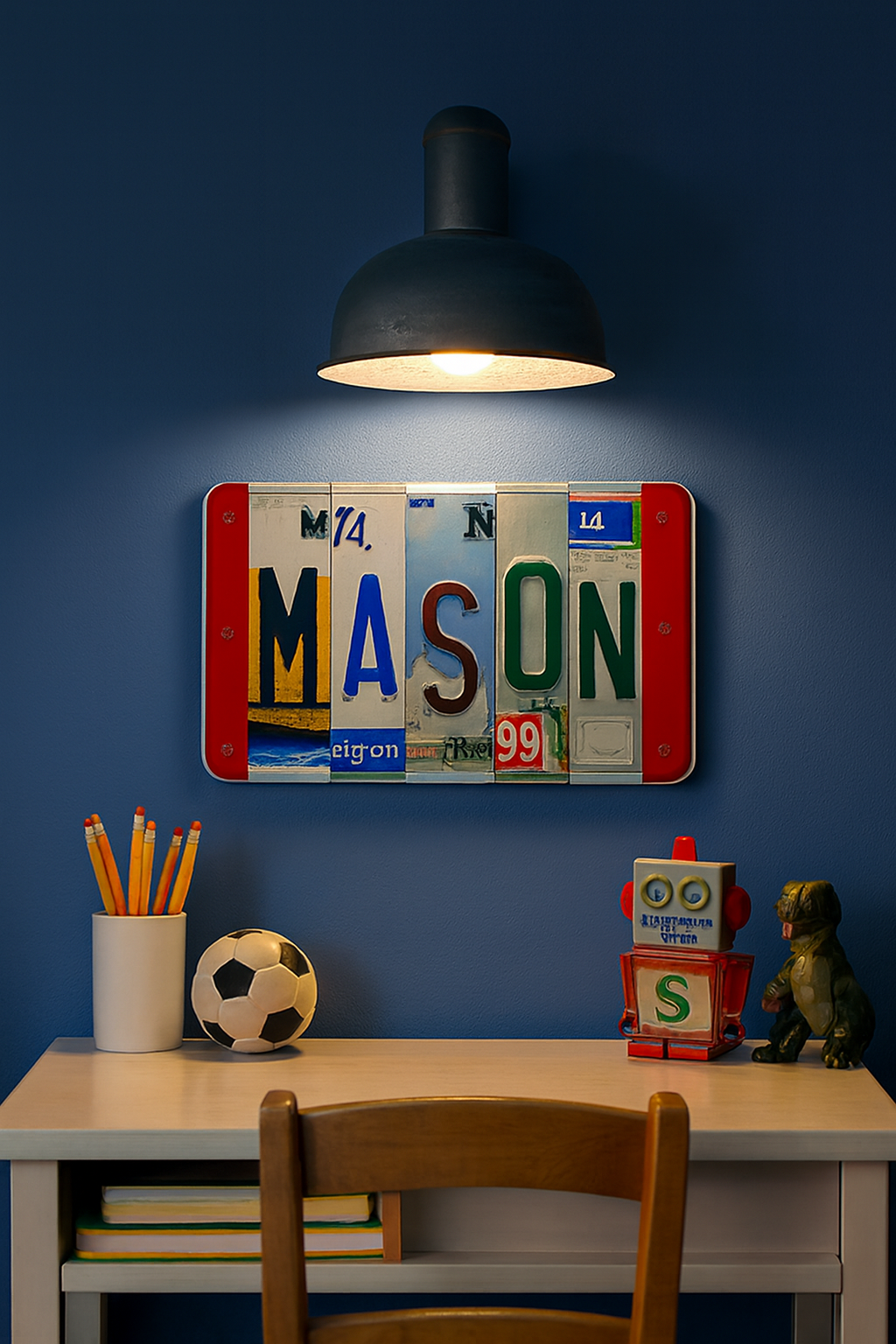 A decorative wall sign made from colorful license plates spelling "MASON" hangs above a desk in a styled room with a blue wall, black pendant lamp, pencils, soccer ball, books, and small toys.