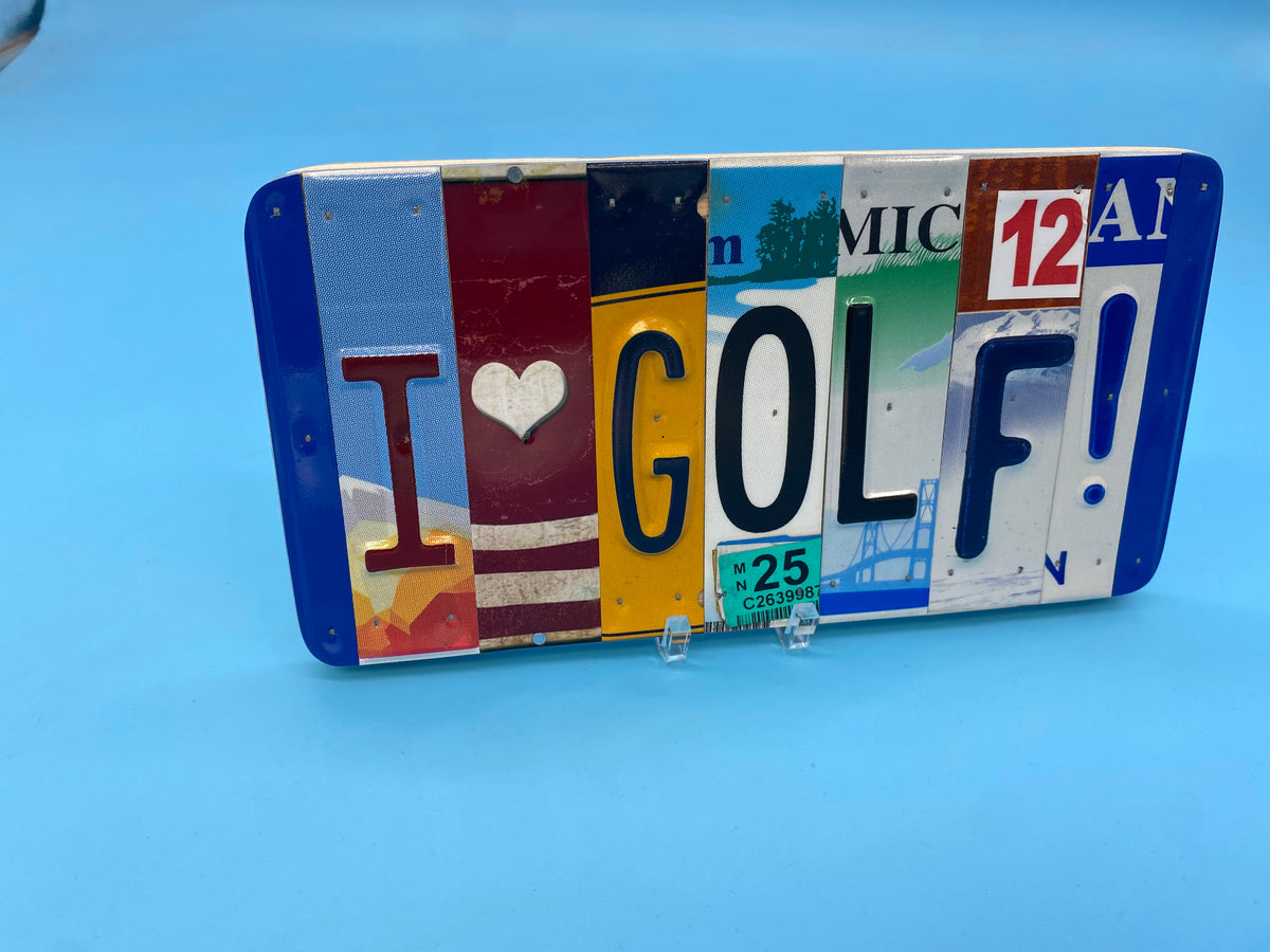 A decorative rectangular sign made from colorful license plates spelling 'I [heart] GOLF!', displayed on small clear stands against a light blue background.