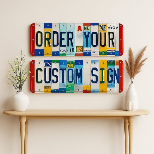 Two rectangular license plate wall signs mounted on a beige wall above a light wood console table. The top sign reads “ORDER YOUR” and the bottom sign reads “CUSTOM SIGN,” each made from colorful license plate strips with red, white, blue, yellow, green, and black lettering.