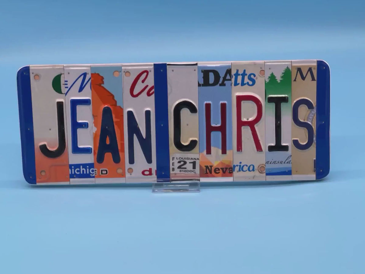 A custom wall sign spelling 'JEAN CHRIS' in raised letters, crafted from various license plates, displayed on a solid blue background.
