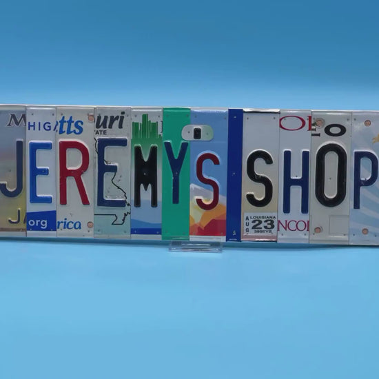 A license plate street sign made from recycled letters JEREMY'S SHOP on a light blue background