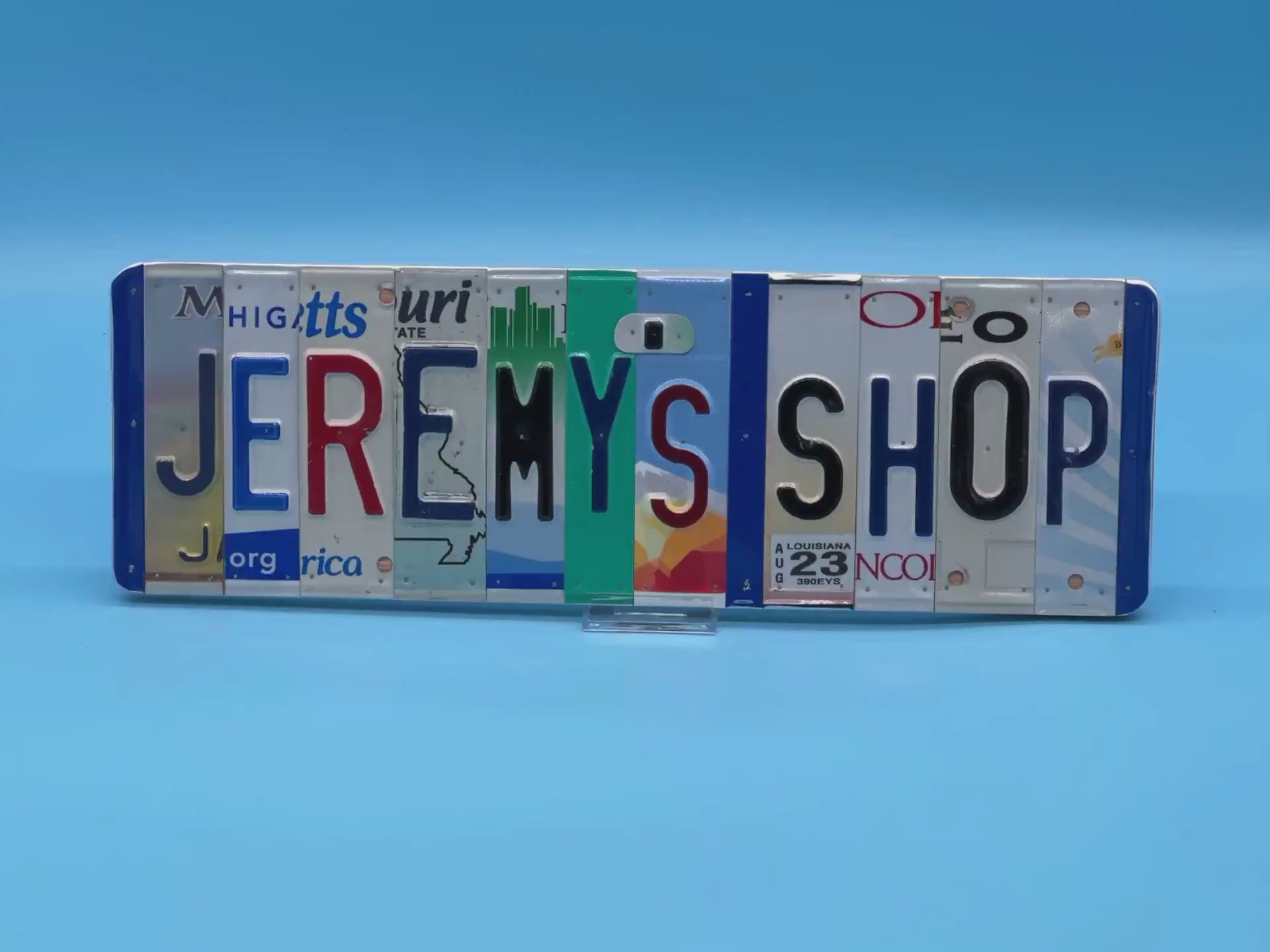 A license plate street sign made from recycled letters JEREMY'S SHOP on a light blue background