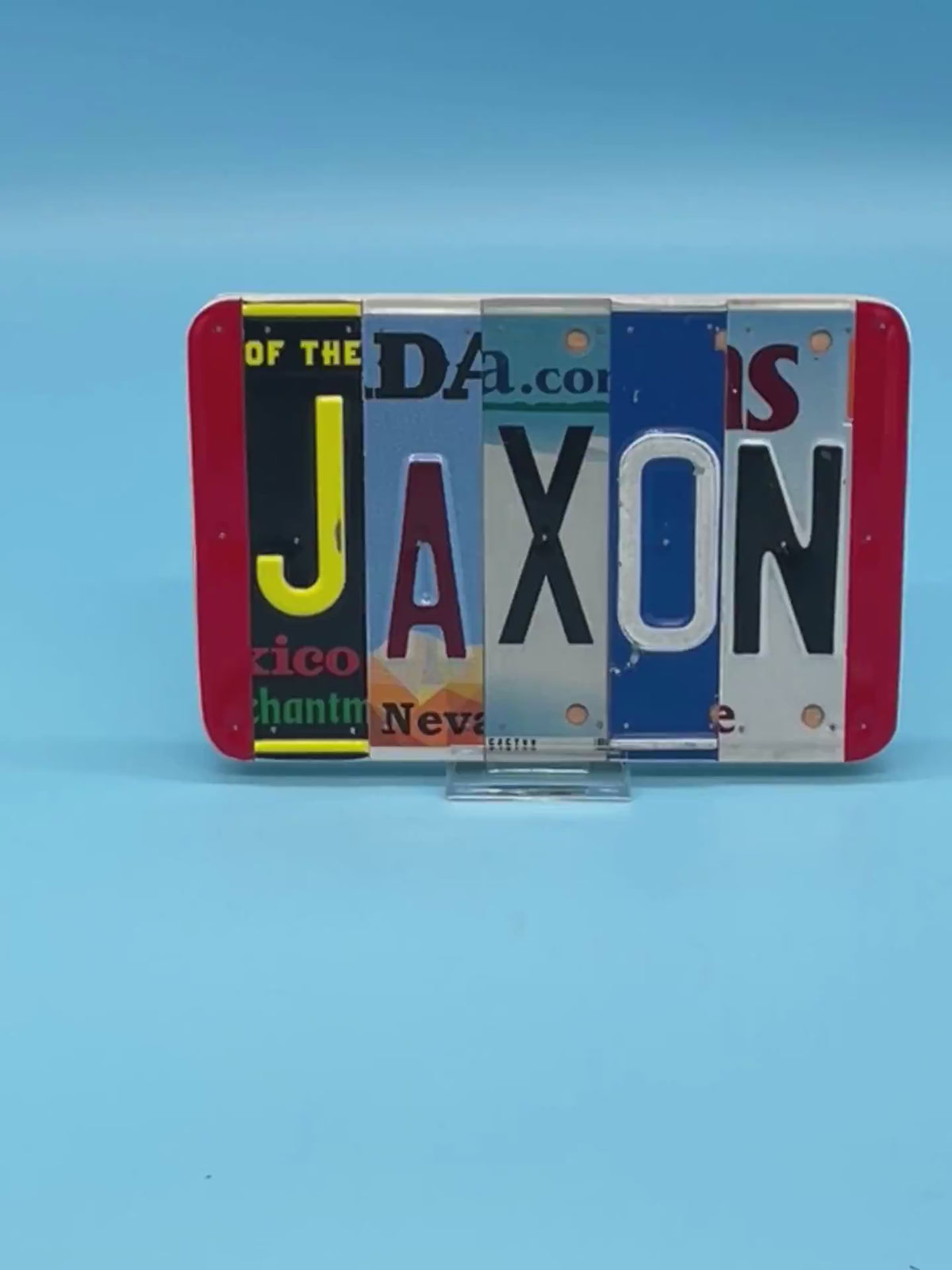 A custom wall sign spelling 'JAXON' in raised letters, crafted from various license plates, displayed on a solid blue background.
